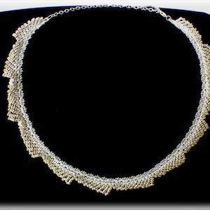 Puede incluir: Un collar de cuentas plateadas y doradas con un diseño en cascada de varios niveles. El collar está hecho de pequeñas cuentas redondas que están dispuestas en un patrón que crea un efecto de onda.