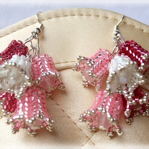 May include: A pair of silver earrings with pink, white, and red beaded flower clusters. The earrings are dangling and have a delicate, feminine look.