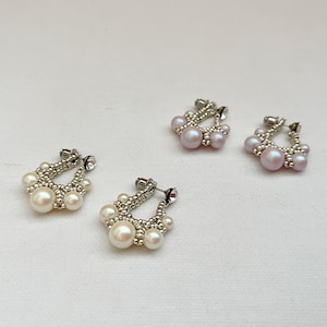 Op de afbeelding: Drie paar parel oorbellen, elk met een zilveren hoepel en een cluster parels. De oorbellen zijn in een rij op een wit oppervlak gerangschikt.