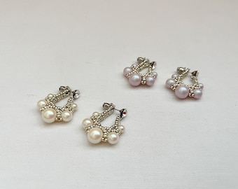 May include: Three pairs of pearl earrings, each with a silver hoop and a cluster of pearls. The earrings are arranged in a row on a white surface.