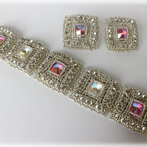 以下が含まれることがあります： 5つの正方形の区画があり、各区画に透明または赤色の虹色のクリスタルが入った銀色のビーズブレスレット。同じデザインのマッチングイヤリングも2つ写っています。