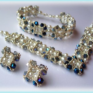 May include: A set of jewellery featuring a necklace, bracelet, and earrings. The jewellery is made with white pearls, clear and blue crystals, and silver beads. The pieces are arranged in a geometric pattern.