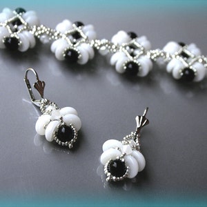 Pode incluir: Um conjunto de joias de contas brancas e pretas que inclui uma pulseira e um par de brincos. A pulseira é feita com pequenas contas brancas e pretas dispostas em um padrão geométrico. Os brincos são brincos pendurados com um design semelhante ao da pulseira.