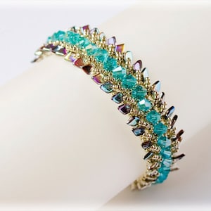 Op de afbeelding: Een gouden en turquoise kralenarmband met een geometrisch ontwerp. De armband is gemaakt met kleine, gefacetteerde kralen die een glinsterend effect creëren.