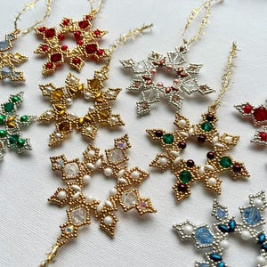 Könnte beinhalten: Nahaufnahme von mehreren Schneeflocken-Ornamenten aus Perlen in verschiedenen Farben, darunter Gold, Rot, Grün und Blau. Jede Schneeflocke hat ein einzigartiges Design und ist mit goldenem Faden zum Aufhängen versehen. Ideal für die Weihnachtsdekoration.