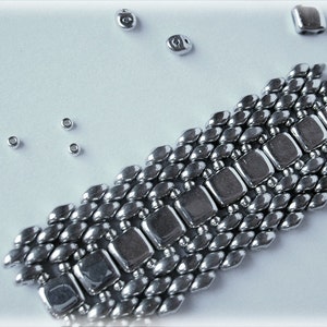 May include: A silver bracelet made of small, square and round beads. The bracelet is made of a repeating pattern of beads.