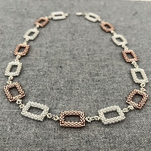 May include: A silver and rose gold necklace with a chain of square links. The necklace is made of small beads and has a delicate look.