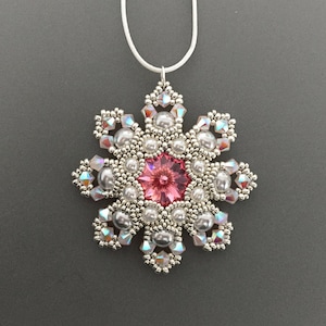 May include: A silver snowflake pendant with a pink crystal center and white pearl accents. The pendant is hanging from a white cord.