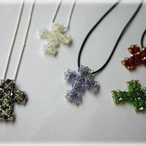 May include: Five beaded cross necklaces with different coloured crystals. The necklaces are on a white surface. The crosses are made of silver and have different coloured crystals, including black, white, purple, red, and green.