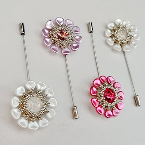 May include: Three beaded flower brooches with silver pins. The flowers are white, pink, and red. Each flower has a silver center with a crystal.