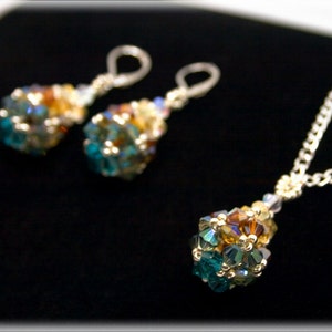 May include: A set of earrings and a necklace with a teardrop-shaped pendant. The jewelry is made of silver and features a cluster of iridescent blue and gold beads.