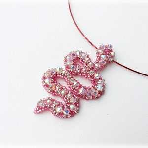 May include: A pink beaded snake pendant necklace with iridescent crystals. The necklace is made with a thin red cord.