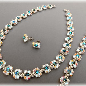 Puede incluir: Un collar y pendientes a juego de plata con cuentas iridiscentes blancas y azules. El collar está hecho de pequeñas cuentas cuadradas dispuestas en un patrón repetitivo.