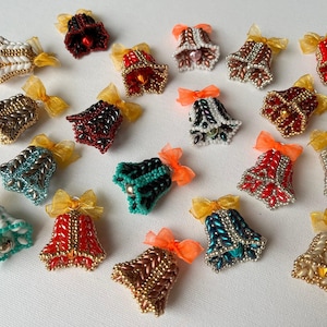 May include: A collection of beaded bell ornaments in various colors, including red, gold, teal, and black. Each bell is adorned with a small bow and a bell-shaped design. The ornaments are arranged on a white surface.