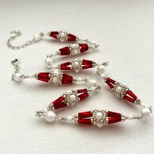 May include: A red and white beaded necklace with a silver clasp. The necklace is made of small, round beads and features a repeating pattern of red and white.