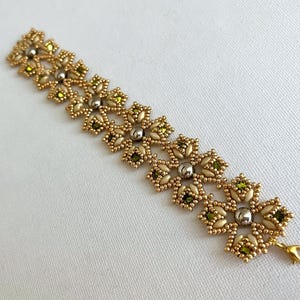 May include: Gold-toned beaded bracelet featuring a floral design with olive green and silver accents. The bracelet has a delicate, intricate pattern and a gold-colored clasp.