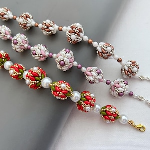 Pode incluir: Três pulseiras de contas em tons de vermelho, verde, branco, rosa e castanho. As pulseiras apresentam intrincados trabalhos de contas, com contas maiores e texturizadas intercaladas com contas menores e pérolas. Cada pulseira tem um fecho.