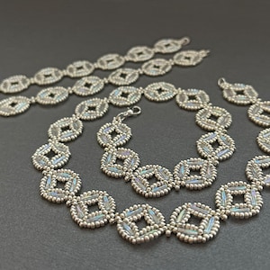 Puede incluir: Tres collares de cuentas plateadas con un patrón geométrico. Los collares están hechos de pequeñas cuentas iridiscentes que crean un efecto brillante.