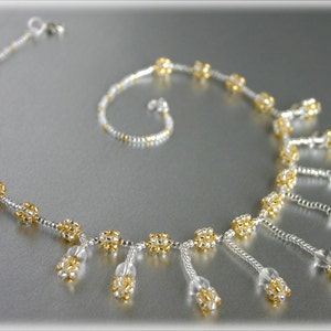 May include: A silver and gold beaded necklace with a delicate design. The necklace features a row of small, round beads with a dangling cluster of beads at the end of each.