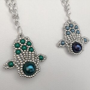 Könnte beinhalten: Zwei silberne Hamsa-Hand-Anhängerketten mit grünen und blauen Perlen und einer schwarzen Perle in der Mitte jedes Anhängers.