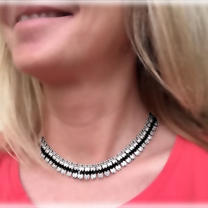 Könnte beinhalten: Eine mehrlagige silberne und schwarze Choker-Halskette mit geometrischem Design.