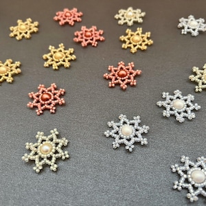 以下が含まれることがあります： 銀、金、赤、ピンクなど、さまざまな色のビーズでできた雪の結晶のオーナメント15個のセットです。それぞれの雪の結晶の中央には真珠のビーズが飾られています。