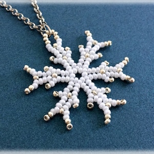 May include: A white and gold beaded snowflake pendant necklace. The snowflake is made of small white beads with gold accents.
