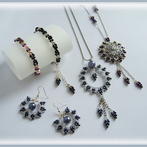 Puede incluir: Un conjunto de joyas de cuentas que incluye un collar, pendientes y dos pulseras. El collar y los pendientes tienen una base de metal plateado con cuentas negras y moradas. Las pulseras son negras y moradas con un acento de metal plateado.