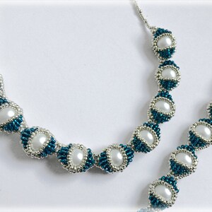Puede incluir: Un conjunto de collar y pulsera de cuentas plateadas y turquesa con detalles de perlas blancas. El collar y la pulsera están hechos con cuentas pequeñas y cuentas redondas más grandes.