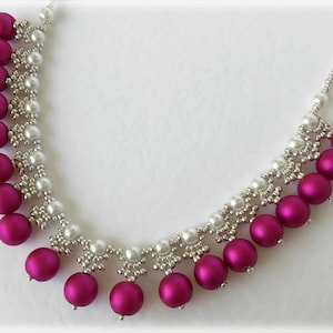 May include: A silver and fuchsia beaded necklace with a graduated design. The necklace features a row of larger fuchsia beads at the bottom, followed by a row of smaller fuchsia beads, and then a row of silver beads.