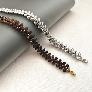 May include: Two leaf-shaped hair clips. One is silver, the other is brown with gold accents. They are arranged diagonally on a grey surface, highlighting their intricate design and metallic finish. These accessories are ideal for adding a touch of nature-inspired elegance to any hairstyle.
