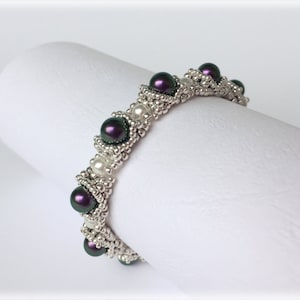 May include: A silver and purple beaded bracelet with a geometric design. The bracelet is made with small silver beads and larger purple beads.