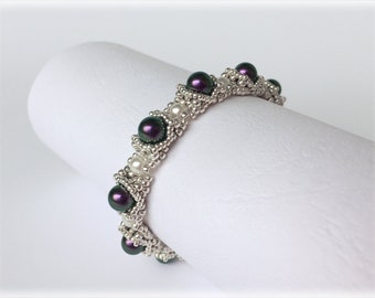 May include: A silver and purple beaded bracelet with a geometric design. The bracelet is made with small silver beads and larger purple beads.