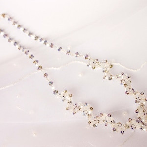 May include: A delicate white beaded necklace with iridescent accents. The necklace features a floral design with small, white beads and purple accents.