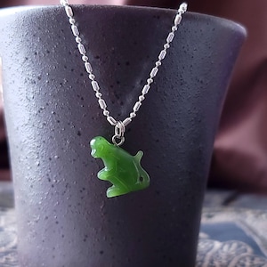 May include: A silver chain necklace with a jade green monkey pendant. The monkey is carved in a sitting position with its arms and legs visible.