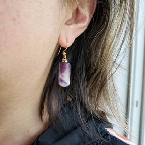 May include: Gold earrings with a purple and white rectangular stone pendant.