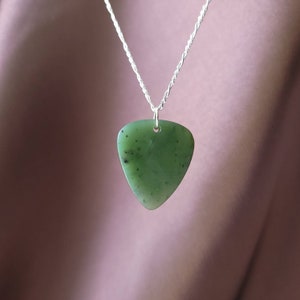 May include: A green jade pendant necklace with a silver chain. The pendant is a triangular shape with rounded edges and small black inclusions. The silver chain is a twisted rope design.