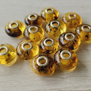 May include: A collection of amber glass beads with silver accents. The beads are round and have a translucent appearance. They are perfect for jewelry making or other craft projects.