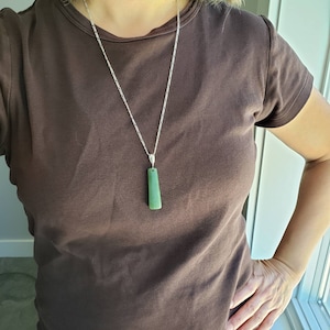 Könnte beinhalten: Eine silberne Kettenkette mit einem grünen Jade-Anhänger. Der Anhänger ist ein langes, dünnes Rechteck mit abgerundeten Kanten.