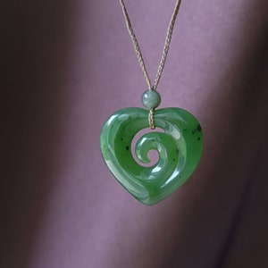 May include: A green jade heart pendant with a carved spiral design, hanging from a brown cord.
