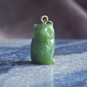 May include: A green jade owl pendant with a gold-colored bail. The owl is carved with detailed feathers and facial features. The pendant is approximately 1 inch tall.