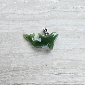 May include: A green jade pendant shaped like a whale, featuring white markings and a silver bail. This whale pendant is a unique piece of jewellery.