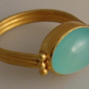 May include: A gold ring with a light blue oval gemstone. The ring has a simple band with three ridges and small gold beads on the side.
