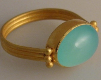 May include: A gold ring with a light blue oval gemstone. The ring has a simple band with three ridges and small gold beads on the side.