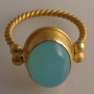 May include: A gold ring with a twisted band and a light blue oval gemstone set in a gold bezel.