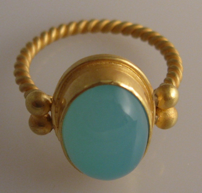 May include: A gold ring with a twisted band and a light blue oval gemstone set in a gold bezel.