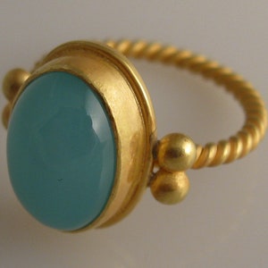 May include: A gold ring with a twisted band and a large, oval-shaped turquoise gemstone set in a gold bezel.