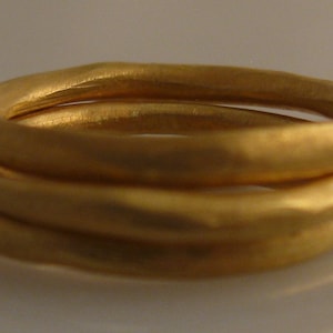 May include: Three gold rings stacked on top of each other. The rings are smooth and have a slightly hammered texture.