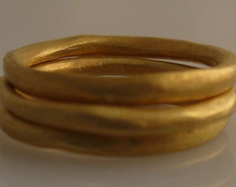 May include: Three gold rings stacked on top of each other. The rings are smooth and have a slightly hammered texture.