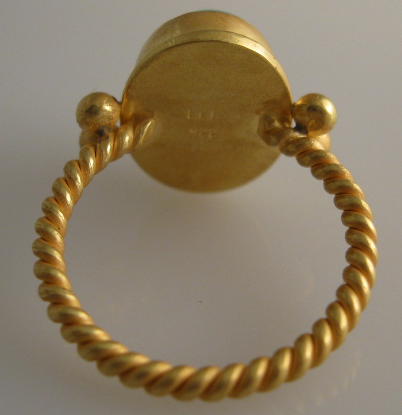 May include: A gold ring with a twisted band and a round green gemstone set in a bezel. The back of the ring has a hallmark.